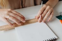 Kaboompics - Designer Measuring a Blank Sketchbook Page with a Wooden Ruler and Pencil