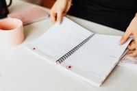 Kaboompics - Hands Turning an Open Planner Beside a Pink Mug on a Desk