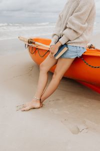 Kaboompics - Vertical Beach Portrait of Barefoot Woman Holding a Book Beside an Orange Kayak