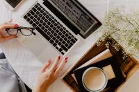 Kaboompics - Woman Reaching for Eyeglasses beside Laptop, Coffee and Books in a Cozy Bedside Workspace