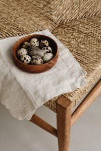 Kaboompics - Quail Eggs And Feather In Wooden Bowl On Woven Chair