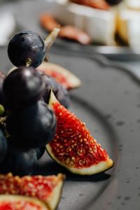 Kaboompics - Single Fig Wedge and Black Grapes on a Dark Plate, Macro