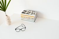 Kaboompics - Black Reading Glasses on Illustrated Books beneath a Palm Leaf