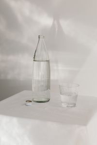 Kaboompics - Minimal Water Bottle and Textured Drinking Glass on a Sunlit White Table, Clean Hydration Background