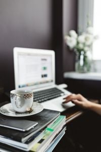 Woman Working From Home On Laptop With Coffee And White Flowers