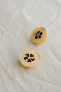 Kaboompics - Two Seeded Japanese Quince Halves on Soft White Linen, Vertical Macro Still Life