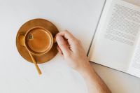 Kaboompics - Hand Reaching for Coffee beside an Open Book