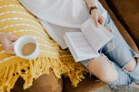 Kaboompics - Woman with a cup of coffee & book, yellow blanket, blue jeans pants