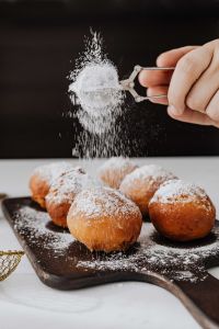 Kaboompics - Hand Dusting Pączki with Sugar on a Dark Wooden Board