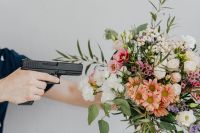 Kaboompics - Hand Holding a Black Handgun Beside a Pink and White Bouquet, Floral Editorial