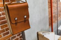 Kaboompics - Closed Tan Leather Portfolio Bag with Buttoned Straps Against a Brick Wall