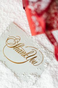 Kaboompics - Gold Foil Thank You Card with a Red Christmas Gift on Textured White Fabric