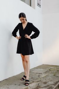 Kaboompics - Asian Woman Looking Down with Hands on Waist in Black Dress by White Wall