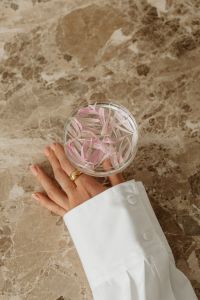 Kaboompics - Hand Holding Glass with Pink Petals over Marble Background