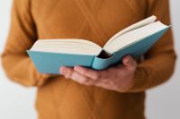 Kaboompics - A man in a brown sweater reading a book, white background