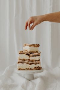 Kaboompics - Hand Reaching Over Stacked Napoleonka Squares on a White Cake Stand