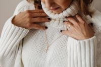 Kaboompics - Cross Necklace Displayed over White Knit Sweater, Hands on Chest