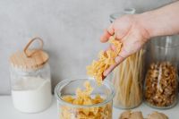 Kaboompics - Hand Pouring Bow-Tie Pasta into a Reusable Glass Pantry Storage Jar