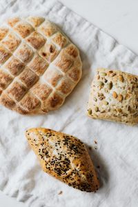 Kaboompics - Scored Slovenian Loaf and Seeded Bun on White Linen, Artisan Bread Food Styling