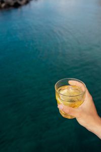 Kaboompics - Hand Holding a Yellow Drink over Teal Sea with Copy Space