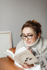 Kaboompics - Woman Reading at Home Wrapped in a Cozy Knit Blanket