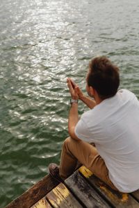 Kaboompics - Back View of Man Sitting on a Wooden Dock with Hands Together and Digital Watch