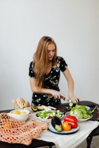 Kaboompics - Home Cook Chopping Cucumber beside Bread Rolls and Salad Ingredients