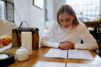 Kaboompics - Blonde Woman Reviewing Cafe Menu at Wooden Table