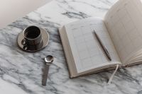 Kaboompics - Vertical Chrome Coffee Cup, Spoon and Open Planner on Marble, Minimal Workspace Copy Space