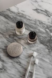 Kaboompics - Skincare Bottles, Silver Compact and Two Toothbrushes on Marble Vanity