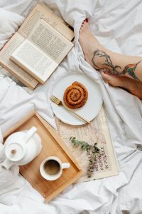 Kaboompics - Woman’s Tattooed Leg beside Cinnamon Roll, Coffee and Open Book in Bed