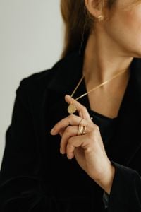 Kaboompics - Woman Holding Gold Pendant Necklace Over Black Blazer