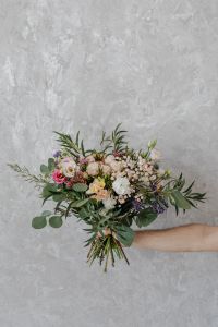 Kaboompics - Hand Holding a Mixed Flower Bouquet against a Textured Gray Wall, Vertical Floral Background