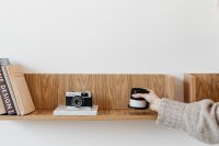 Kaboompics - Hand Placing Black Candle Beside Vintage Camera on Wooden Shelf