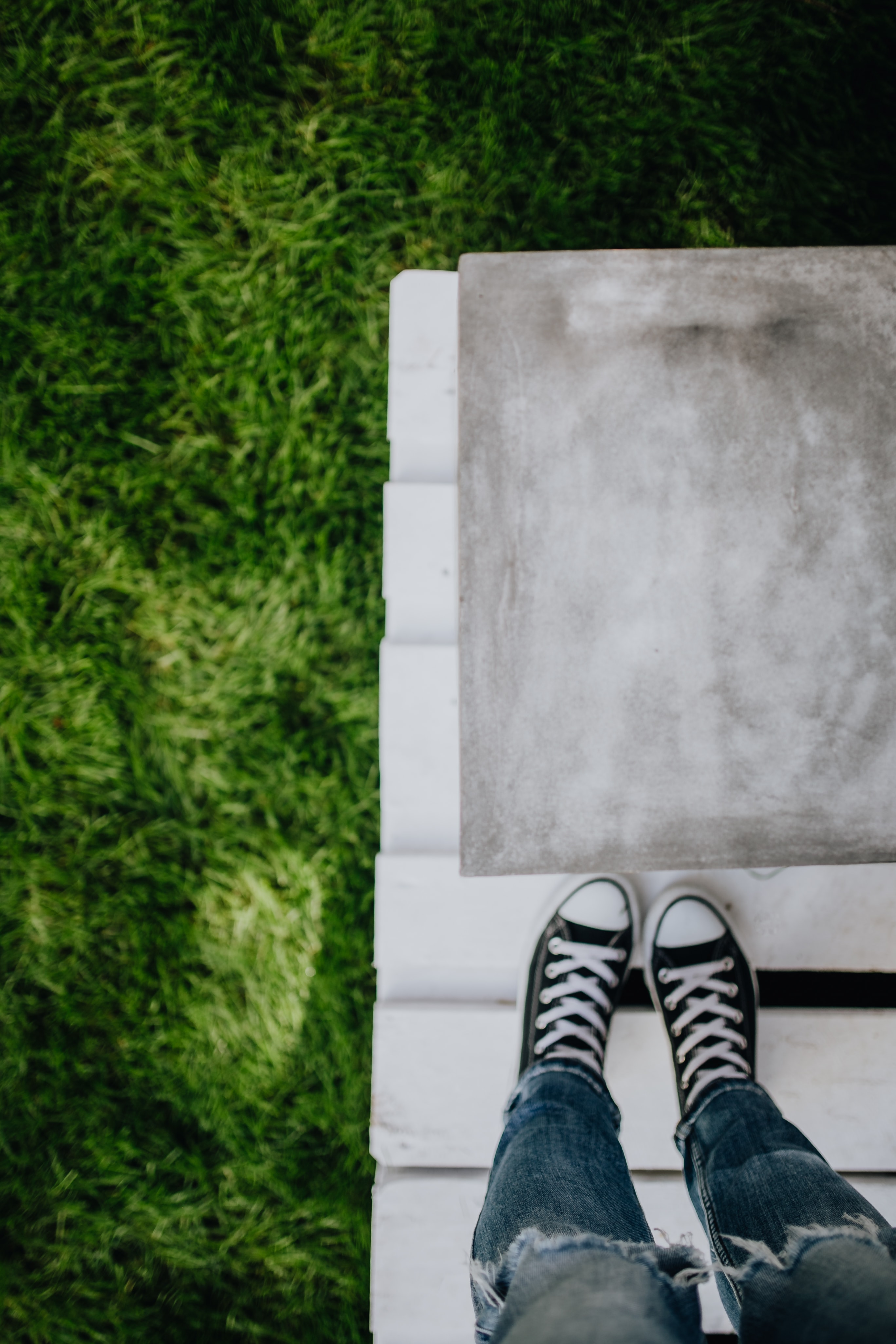 Concrete side table and green grass in garden, woman, jeans, sneakers