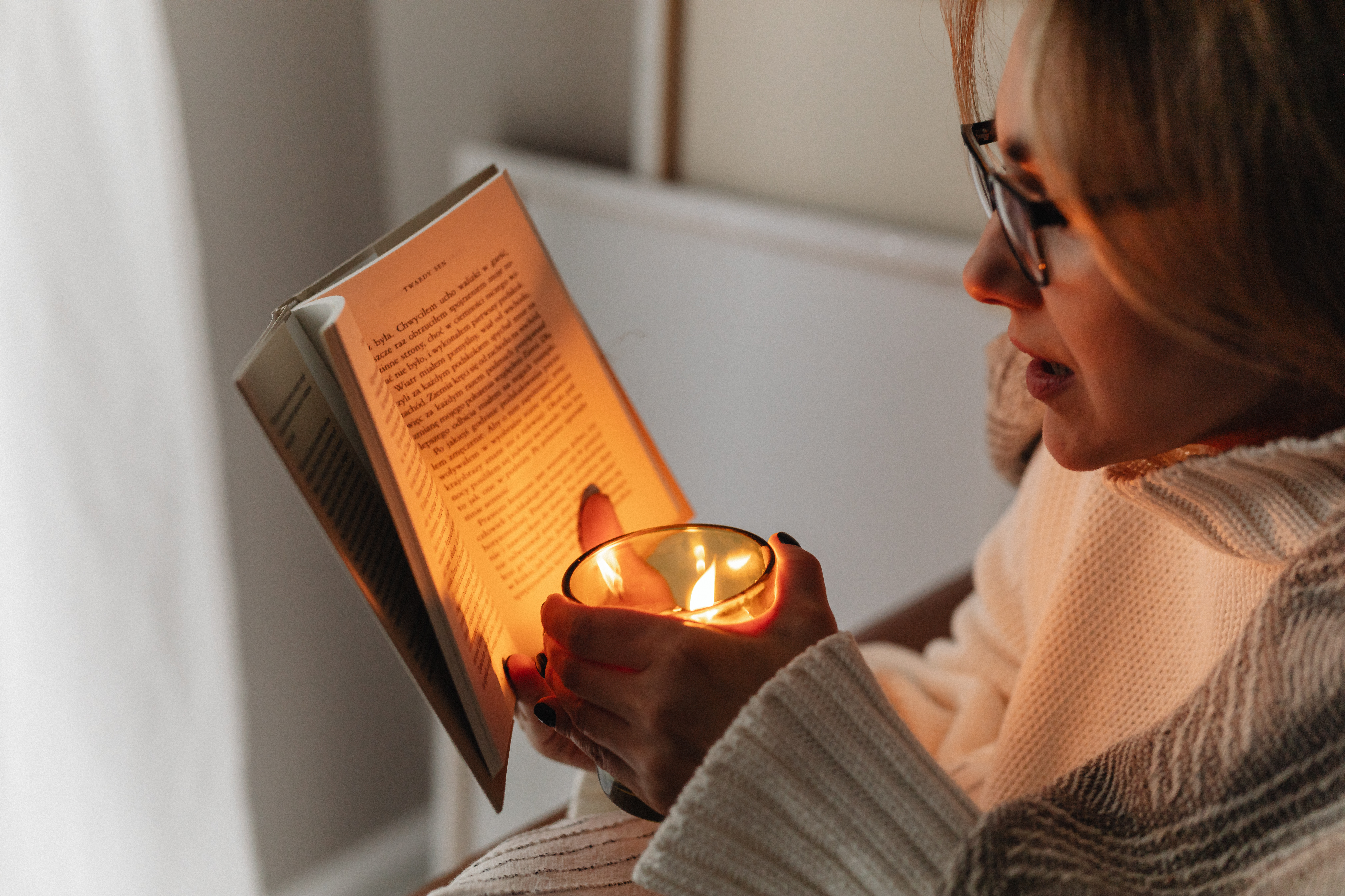 A woman holds a burning candle in her hands - reading a book