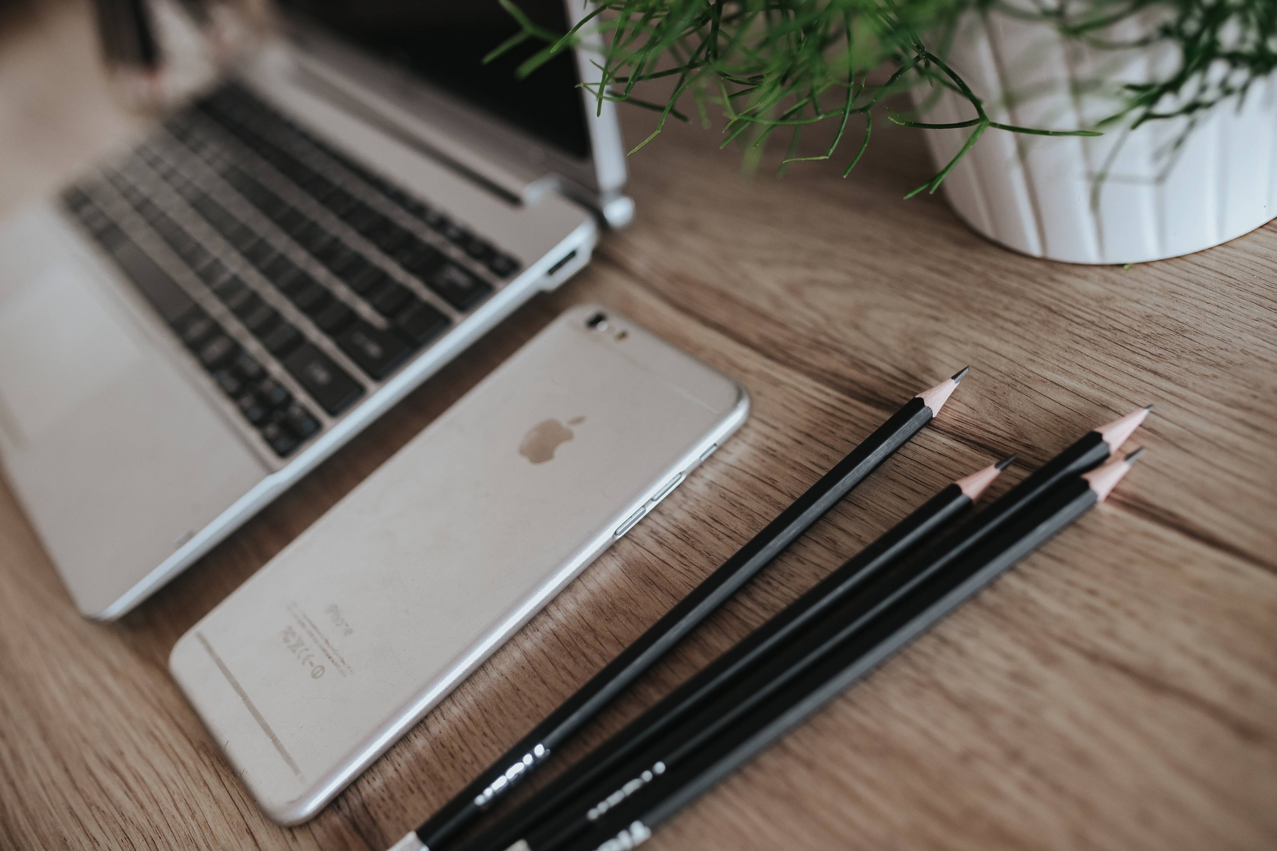 Silver Acer laptop on a wooden desk with a green plant, pencils and an Apple iPhone