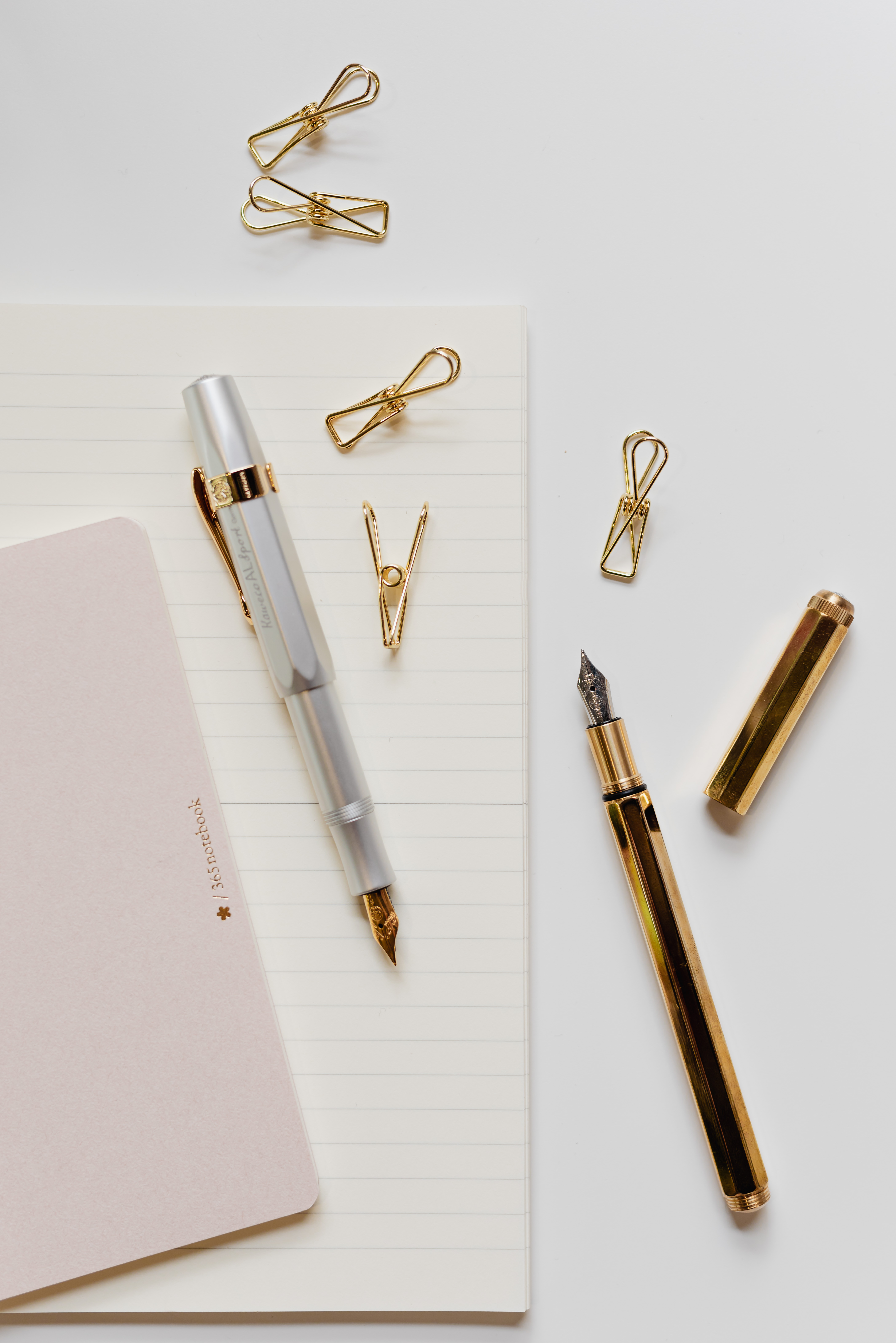 Fountain pens, clips and notebooks on a white desk