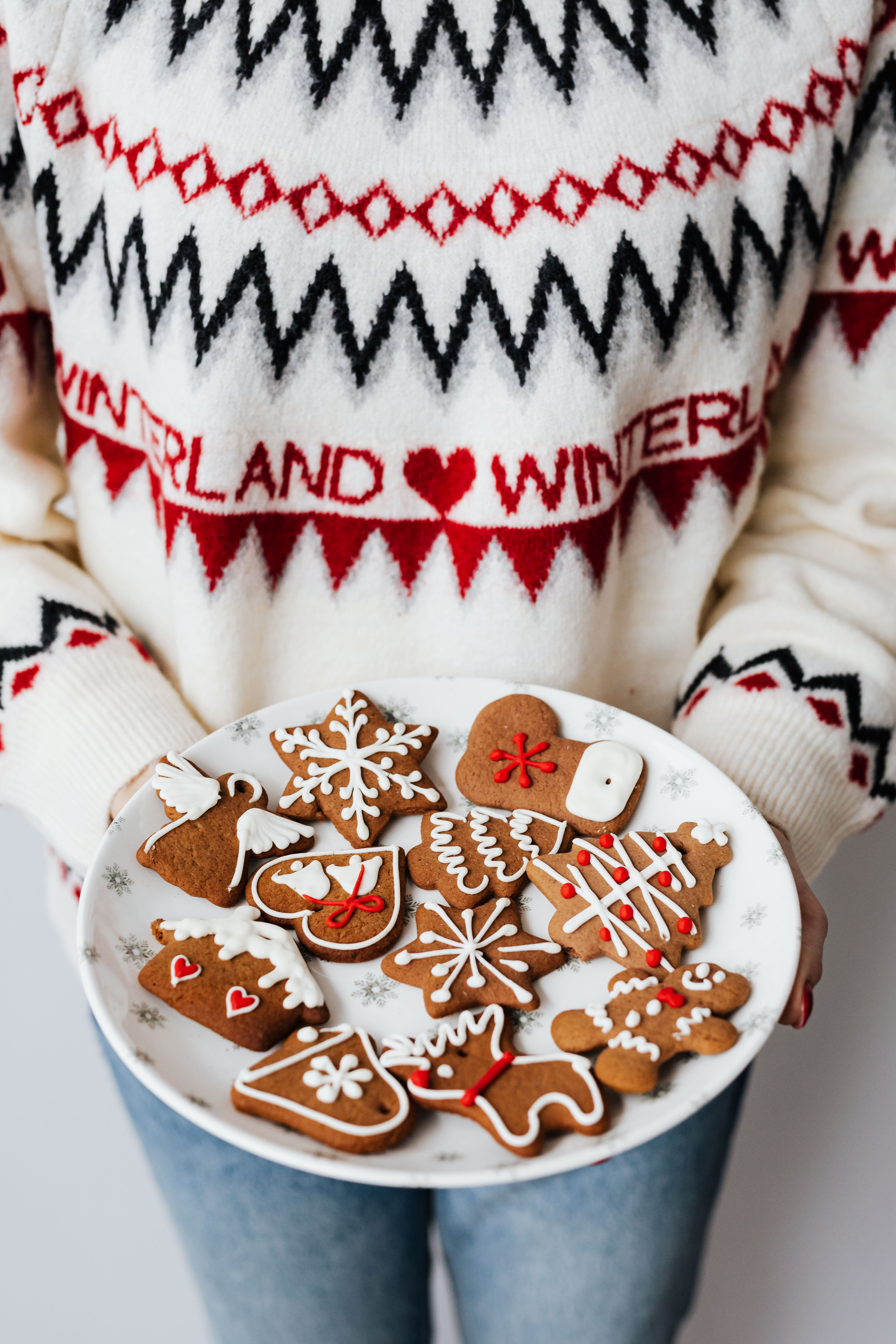 Woman in a white Christmas sweater holds gingerbread cookies on plate