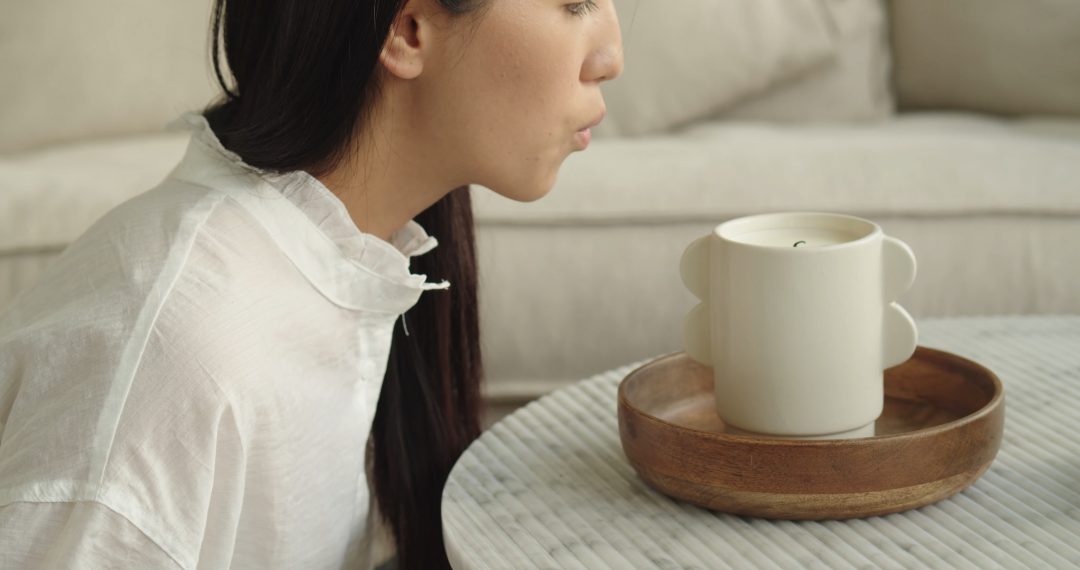 Woman Sitting Next to a Burning Candle, Blowing Out a Candle