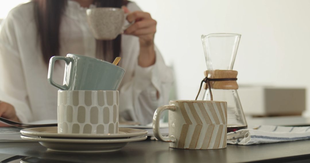 Kitchen Table with Tea and Coffe Cups and Woman Drinking Coffee in the Background