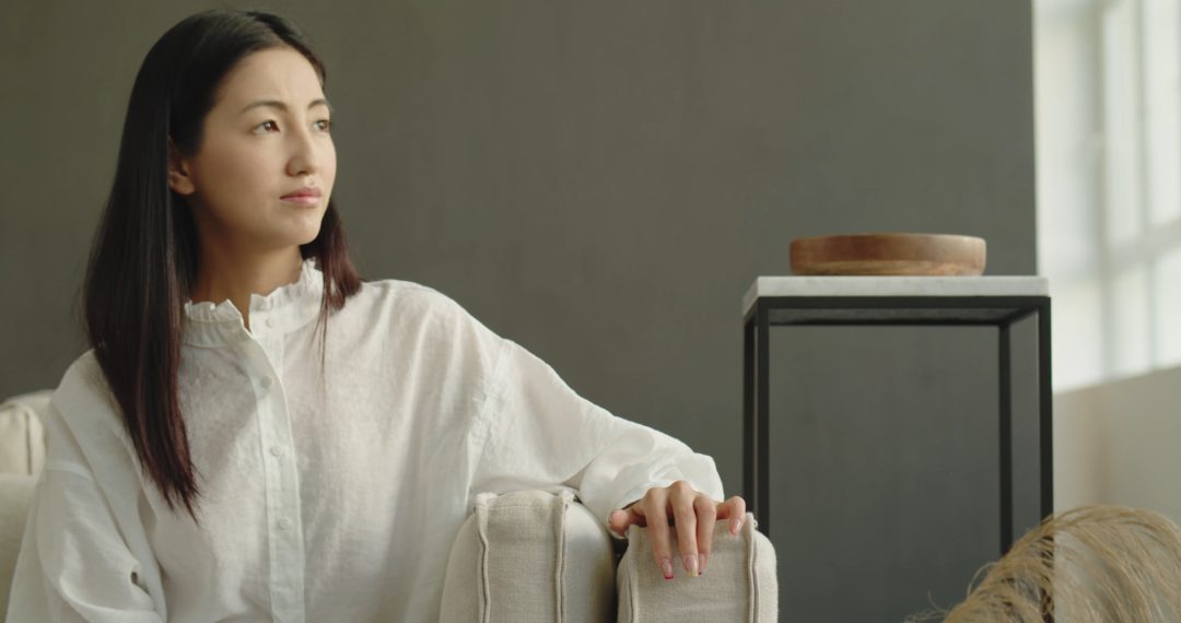 Thoughtful Woman Sitting on the Couch, Looking Off Into the Distance, Drumming her Fingers