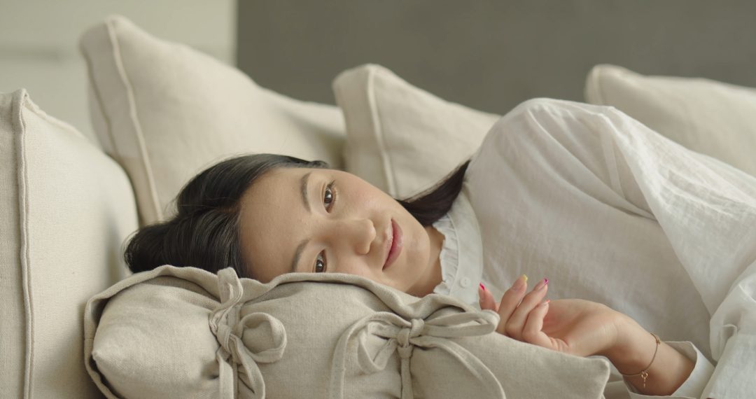 Tired Woman Puts a Pillow on a Couch and Lies Down